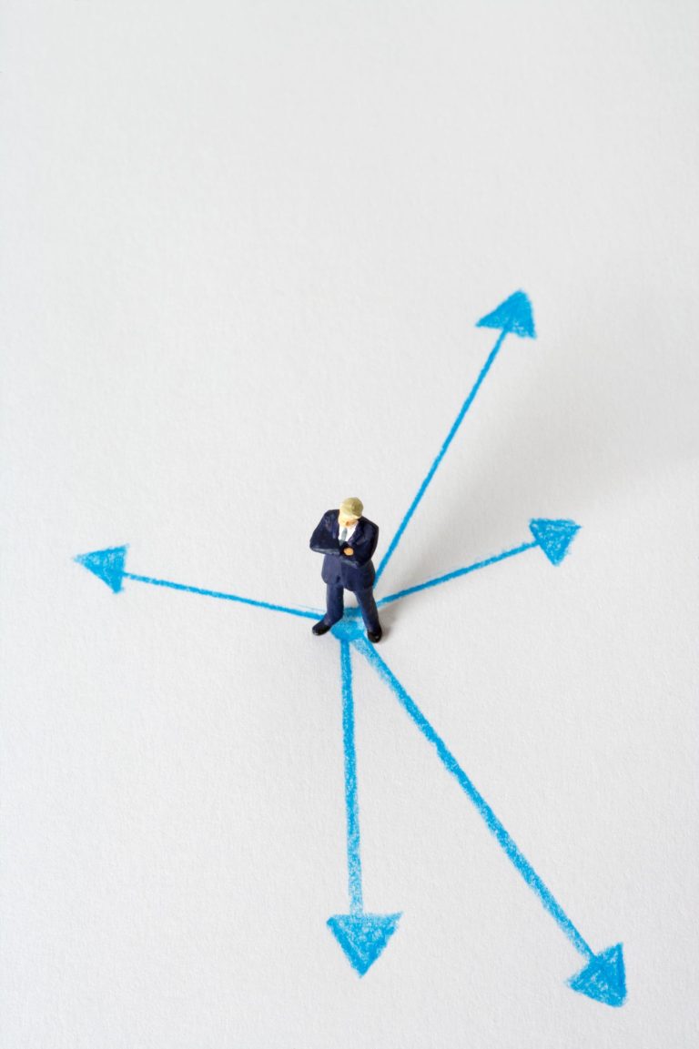 Miniature figure standing at a crossroads of arrows, symbolising a business software choice